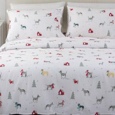 a bed covered in white sheets with dogs and trees printed on the sheet set, along with matching pillow cases