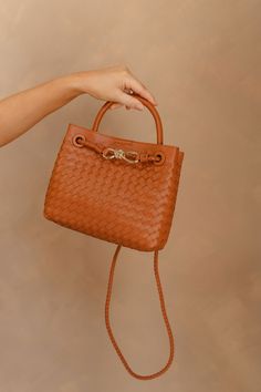 Meet our Blakely Light Brown Braided Purse, a fusion of style and functionality designed to elevate your everyday look. Crafted with a light brown faux-leather woven body, this purse exudes understated elegance. The small handle and braided crossbody strap offer versatility, allowing you to carry it with ease and style. Accentuating its charm is a sophisticated gold detail on the front, adding a touch of luxe to your ensemble. The magnetic closure ensures quick access to your essentials while ke Versatile Brown Bag With Braided Handles, Chic Brown Leather Woven Bag, Chic Cognac Shoulder Bag With Braided Handles, Chic Brown Bag With Intrecciato Weave, Chic Brown Bags With Intrecciato Weave, Trendy Brown Woven Leather Bags, Brown Braided Crossbody Bag, Chic Brown Braided Shoulder Bag, Versatile Brown Woven Leather Shoulder Bag