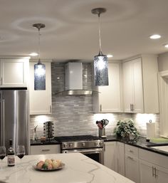 a modern kitchen with white cabinets and marble counter tops, stainless steel appliances and pendant lights