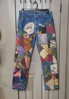 a pair of blue jeans with patches and buttons on them hanging from a white door