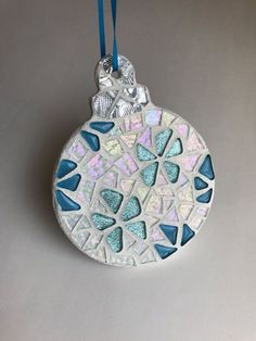 a ceramic ornament hanging from a blue cord on a gray surface with small pieces of glass embedded in it