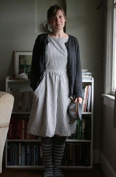 a woman standing in front of a window wearing a striped dress and black cardigan