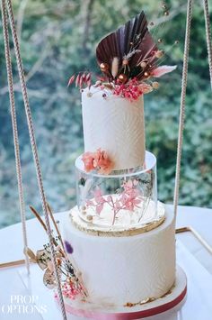 a three tiered wedding cake with flowers and feathers on the top is sitting on a table