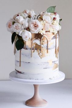 a white cake with flowers on top and gold drips in the middle, sitting on a table