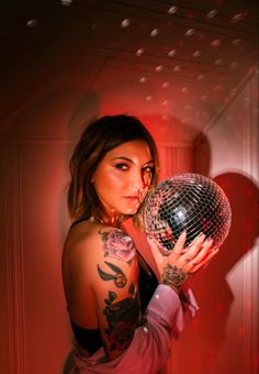 a woman holding a disco ball in her hand and posing for the camera with red light behind her