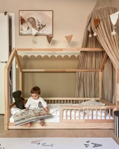 a little boy that is sitting in a bed with a teddy bear on the floor