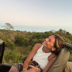 a woman sitting in the back of a truck on top of a lush green field