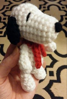 a hand holding a small crocheted dog with a red scarf around it's neck