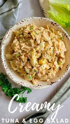 a white bowl filled with tuna and egg salad on top of a table next to lettuce