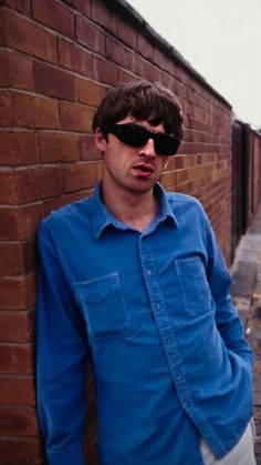 a man wearing sunglasses leaning against a brick wall