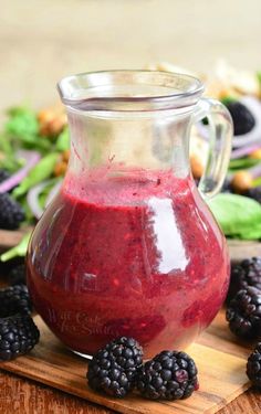 a glass pitcher filled with raspberry sauce on top of a wooden cutting board