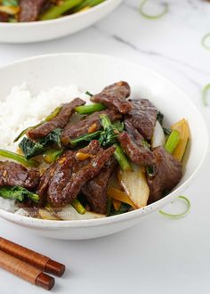 two bowls filled with beef and vegetables on top of rice next to chopsticks