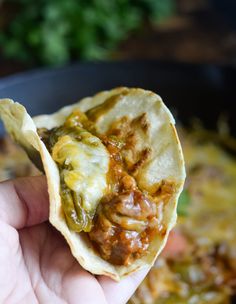 a hand holding up a tortilla filled with meat and cheese in a skillet