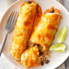 two enchiladas on a white plate with lime wedges next to it