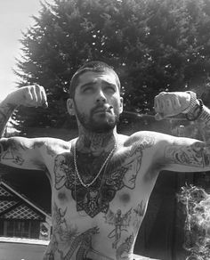 a man with tattoos on his arms and chest standing in front of a fence holding a bottle