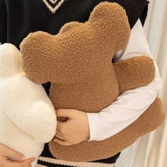 a person holding a brown teddy bear in their arms and wearing a black sweater with white sleeves