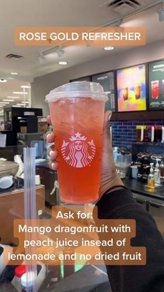 a person holding up a drink in front of a counter with the caption, rose gold refresher ask for mango dragonfruit with peach juice instead of lemonade and no dried fruit