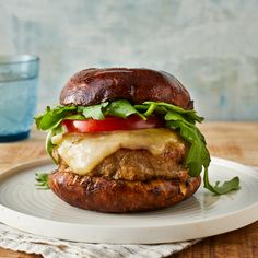 a hamburger with lettuce, tomato and cheese on a plate next to a glass of water