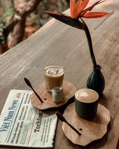 a wooden table topped with a cup of coffee next to a drink on top of a coaster