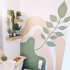 a bathroom with a toilet, sink and green plant wall decals on the walls