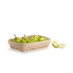 a wooden basket filled with green apples next to an apple slice on a white background