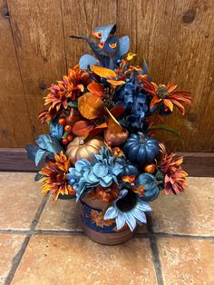 a vase filled with blue and orange flowers on top of a tile floor next to a wooden door