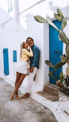 a man and woman standing next to each other in front of a white building with blue shutters