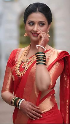 a woman in a red and gold sari with her hands on her face, posing for the camera