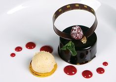 a white plate topped with a chocolate covered dessert and garnished with red sauce