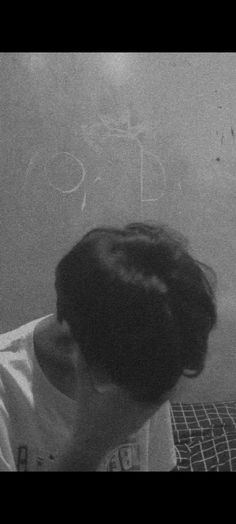 a boy sitting on a bed with his head in his hands and writing on the wall behind him