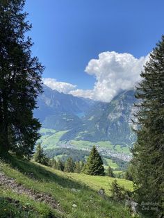 the mountains are covered in green grass and trees, with some clouds above them on a sunny day