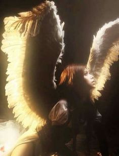 a woman with angel wings on her body in front of a light shining through the darkness