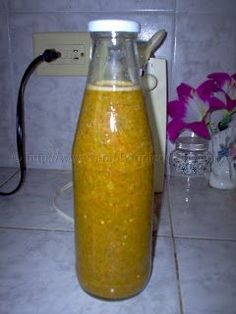 a glass bottle filled with yellow liquid sitting on top of a counter next to a flower