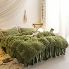 the bed is made up with fluffy green blankets and pillows on it's sides