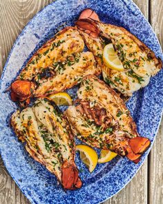 grilled lobsters with lemon wedges and herbs on a blue plate over wooden table