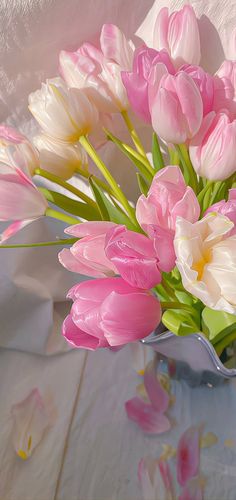 pink and white tulips are in a glass vase on a tableclothed surface