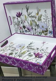 an open purple and white box sitting on top of a wooden table with flowers painted on it