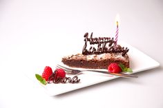 a piece of chocolate cake on a plate with two raspberries