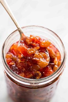 a glass jar filled with fruit jam on top of a white countertop next to a wooden spoon