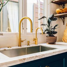 a kitchen sink with brass faucets and marble counter tops in front of a window