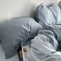 an unmade bed with two pillows and a book on the floor next to it