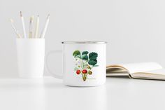 a coffee mug with strawberries on it next to an open book and pencils