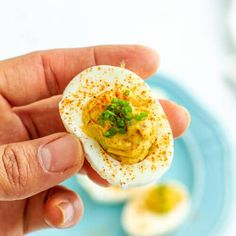 a hand holding an open hard boiled egg with mustard and chives in it on a blue plate