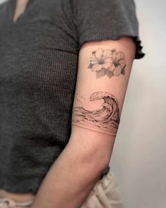 a woman's arm with a wave and flowers tattoo on the left side of her arm