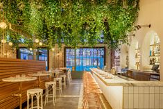 the interior of a restaurant with wooden tables and white stools covered in green vines