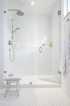 a white tiled bathroom with a walk in shower next to a bench and towel rack