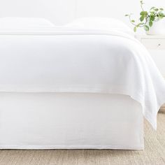 an unmade bed with white linens and a plant on the nightstand next to it