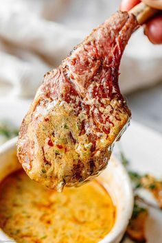 a person is holding up a piece of meat over a bowl of dip and sauce