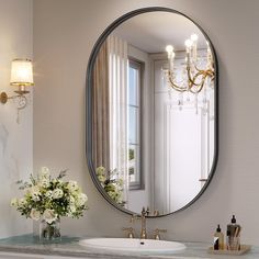 a bathroom sink sitting under a round mirror next to a vase with flowers on it