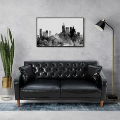 a living room with a black leather couch and potted plant on the floor next to it